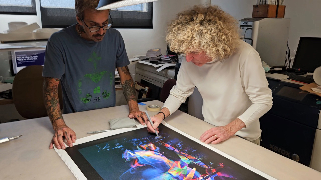 Tommy Aldridge reviewing and signing a canvas with a member of the studio team